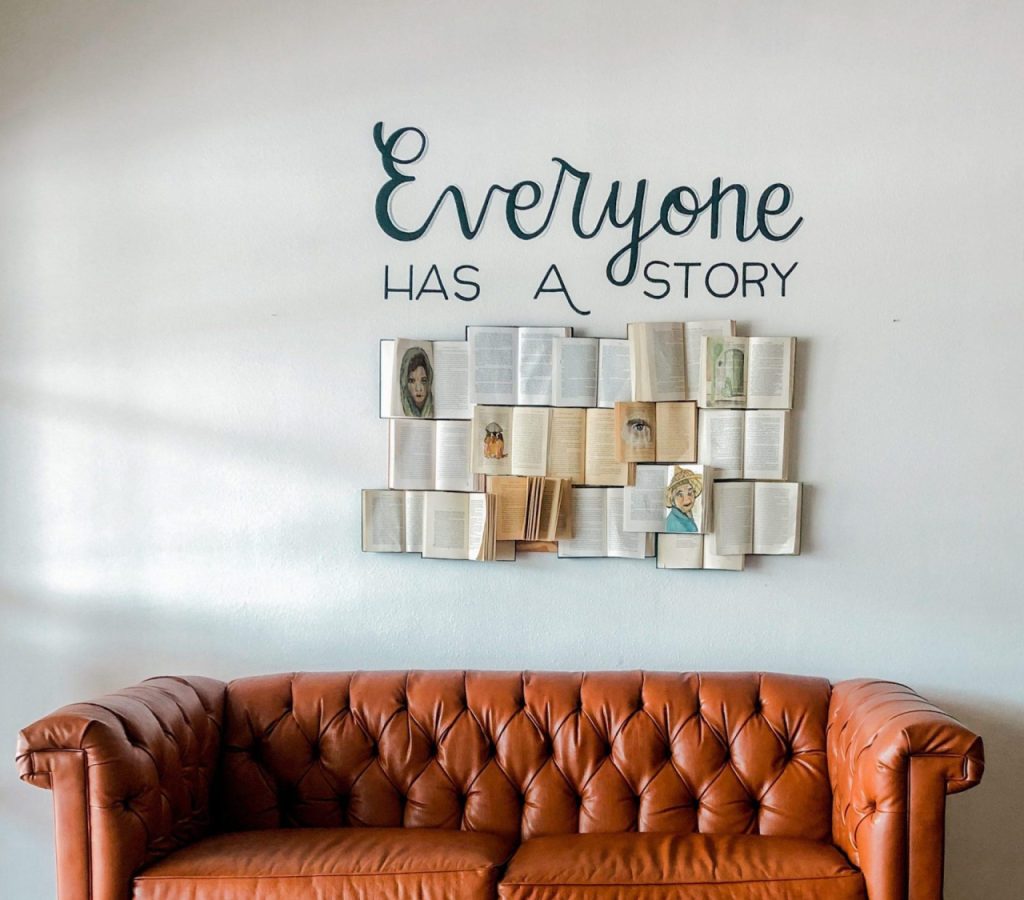 Braune Couch vor weißer Wand mit Büchern und der Aufschrift "Everyone has a story"